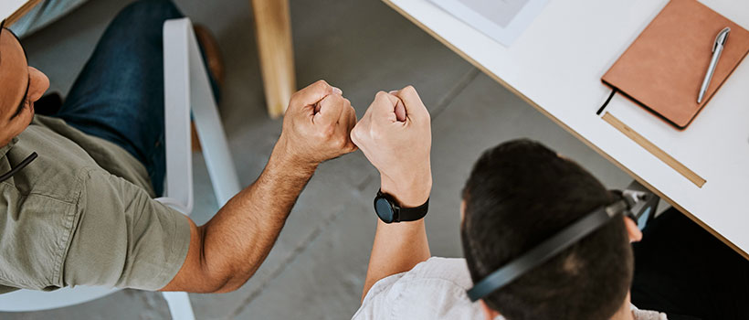 A photo of two employees seated at a table bumping their fists.