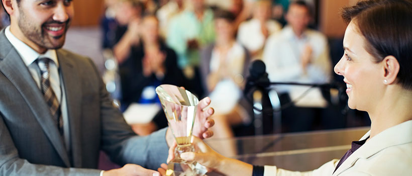 A photo of a woman handing an award to an employee in front of a crowd.