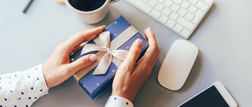 A photo of an employee holding a gift on their computer workspace.