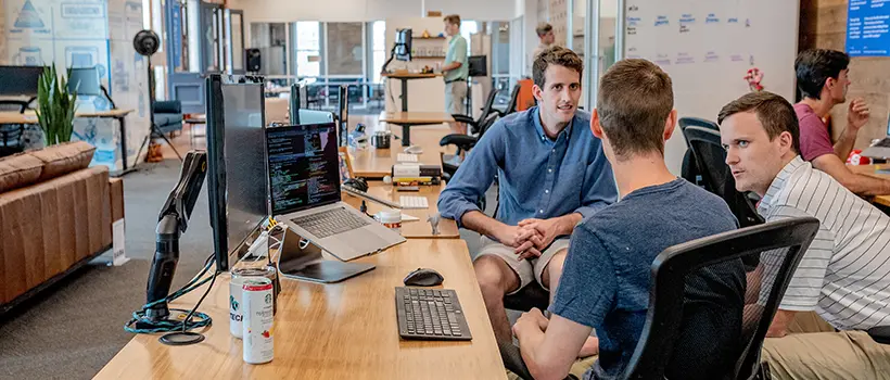 A photo of employees seated at their desks having a meeting. 