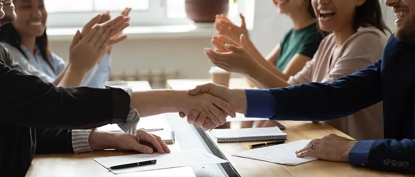 A photo of individuals at a conference table shaking hands.