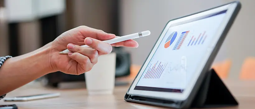 A photo of a person using a pen to point at a tablet with graphs