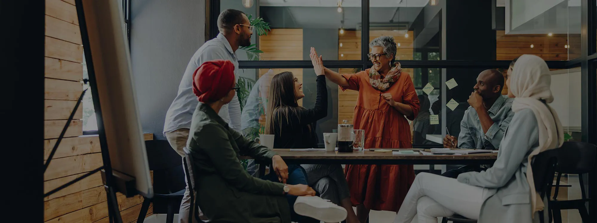 A photo of a team at a conference table with 2 team members slapping each other five.